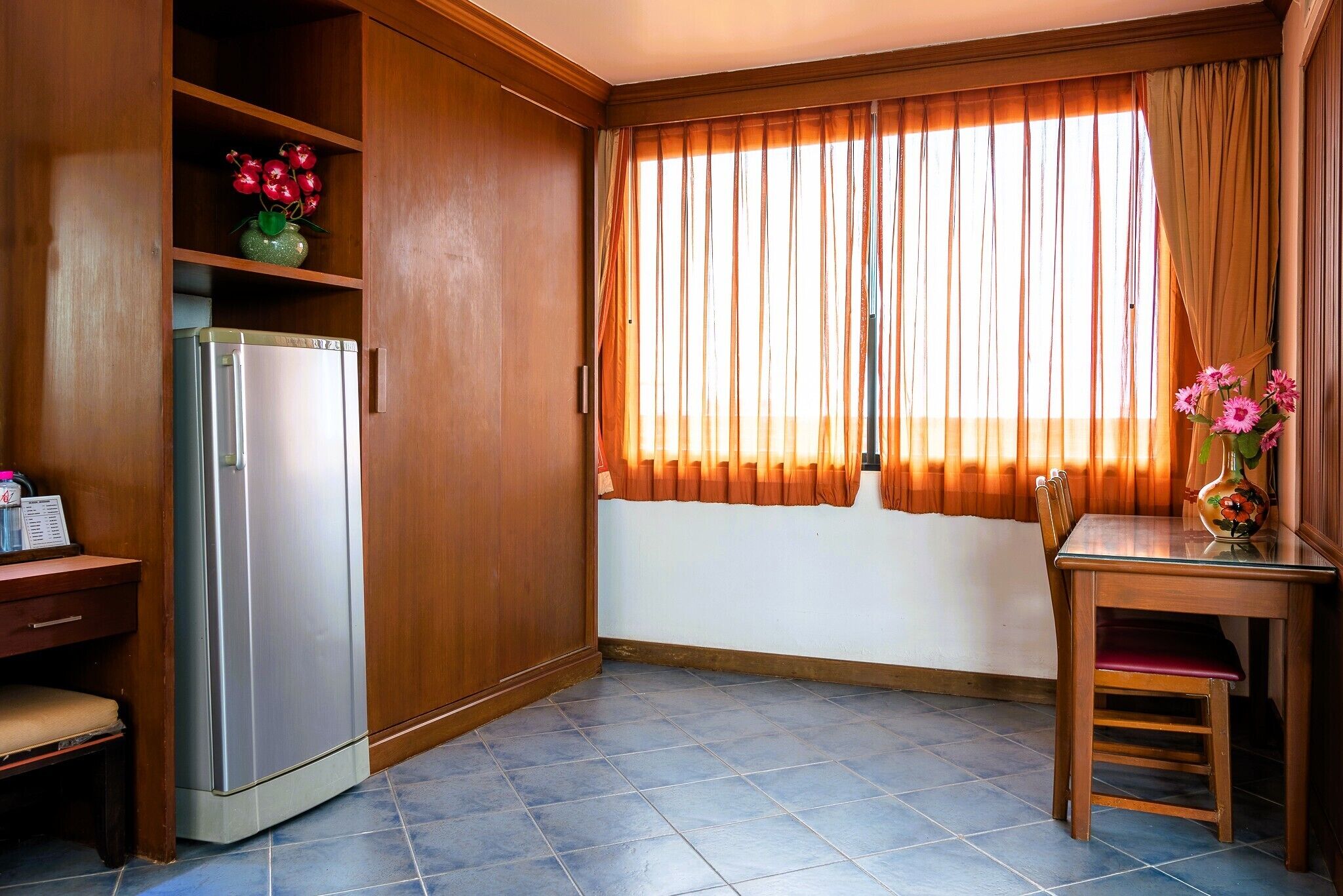 Eine kompakte Küche mit Kühlschrank, Holzschränken, einem Esstisch mit Stühlen und einem Fenster mit Vorhängen.