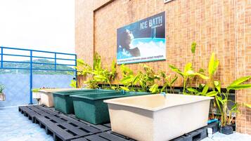 Uma área no terraço com banheiras de imersão em água gelada, um corrimão azul e plantas em vasos.