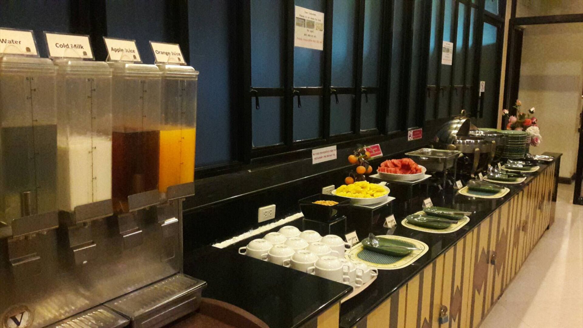 A buffet with labeled dispensers for water, cold milk, apple juice, and orange juice.