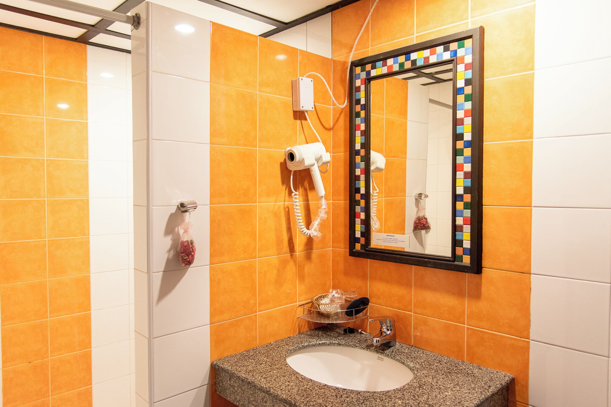 Ein Badezimmer mit orangefarbenen Fliesen, einem Granitwaschbecken, einem Spiegel mit farbigem Rahmen und einem an der Wand befestigten Fön.
