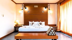 Una habitación de hotel con una cama grande, lámparas de noche, una mesita de noche y una mesa de madera.