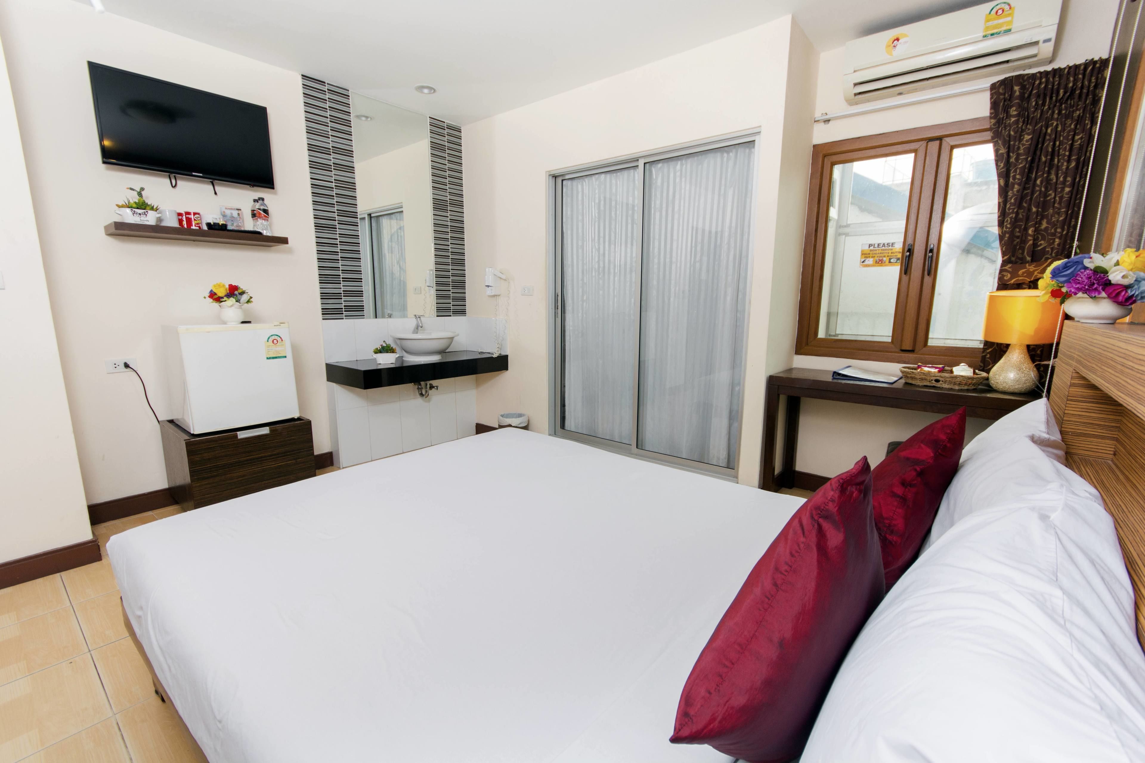 A hotel room with a bed, a TV mounted on the wall, a small fridge, a sink, and a window with curtains.