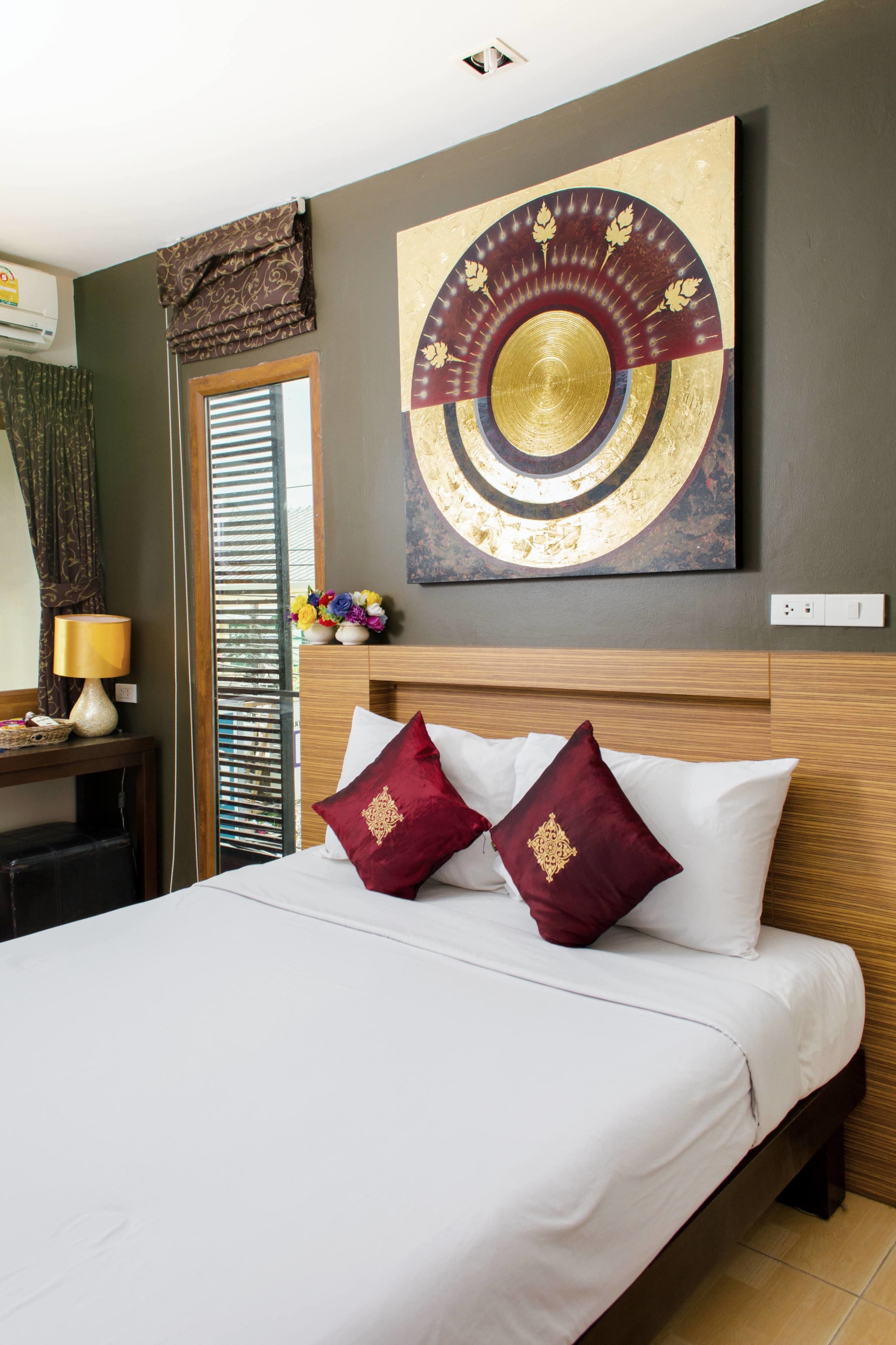 A hotel room with a bed, a nightstand with a lamp, a wall-mounted artwork, and a window with curtains.