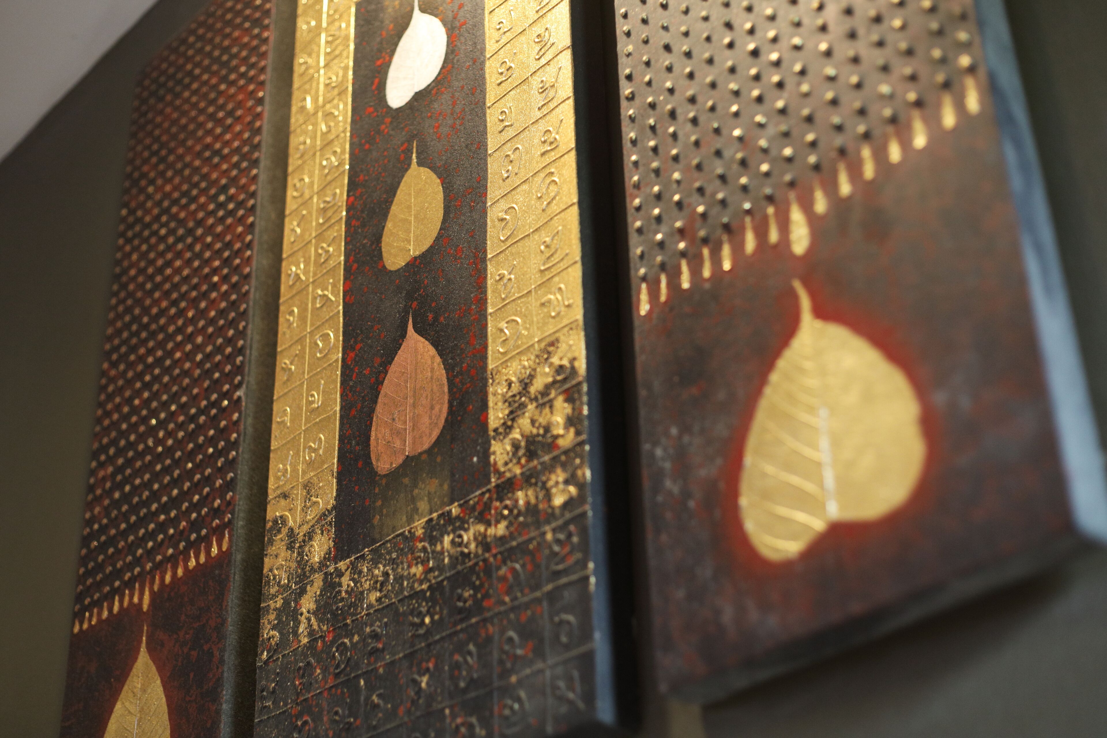 A close-up of a textured wall with a pattern of gold and black tiles, featuring leaf motifs.