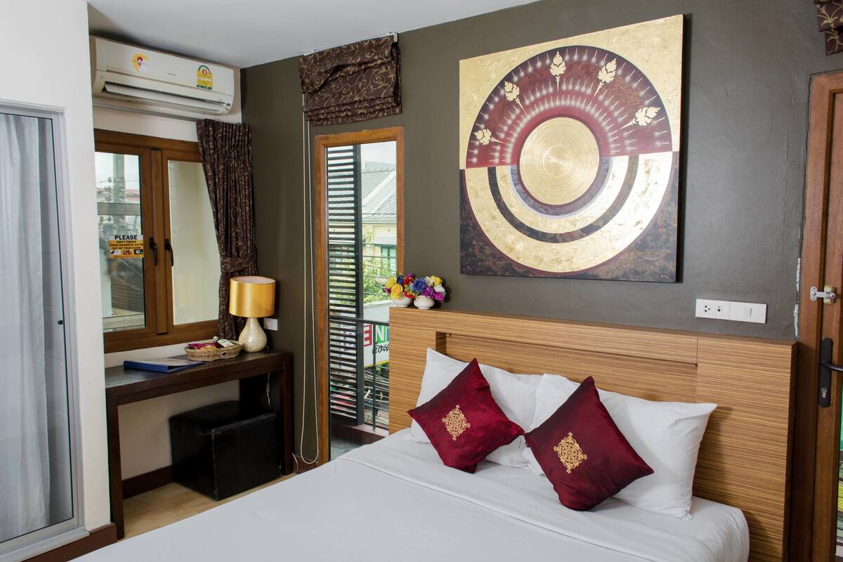 A hotel room with a bed, a desk with a lamp, a large wall art piece, and a window with curtains.