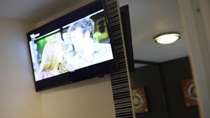 A television mounted on a wall displaying a scene with two people. - Sleep With Inn (Bangkok)