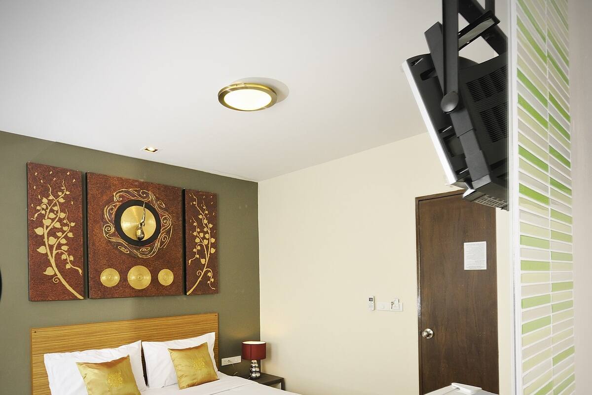A hotel room with a bed, a bedside table with a lamp, a wall clock, and a radiator.
