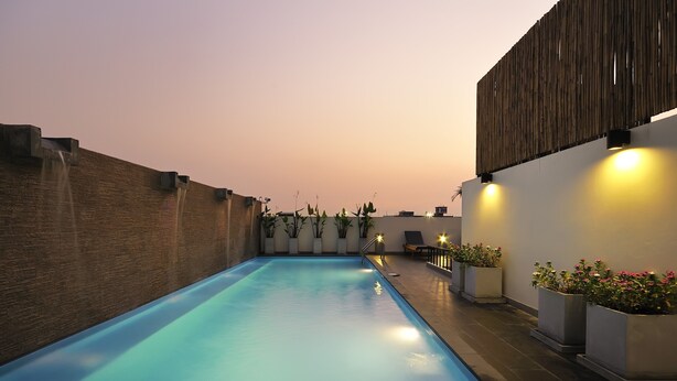 A swimming pool with a brick wall on one side and a white wall on the other, with potted plants and lights along the pool's edge. - Sleep With Inn (Bangkok)