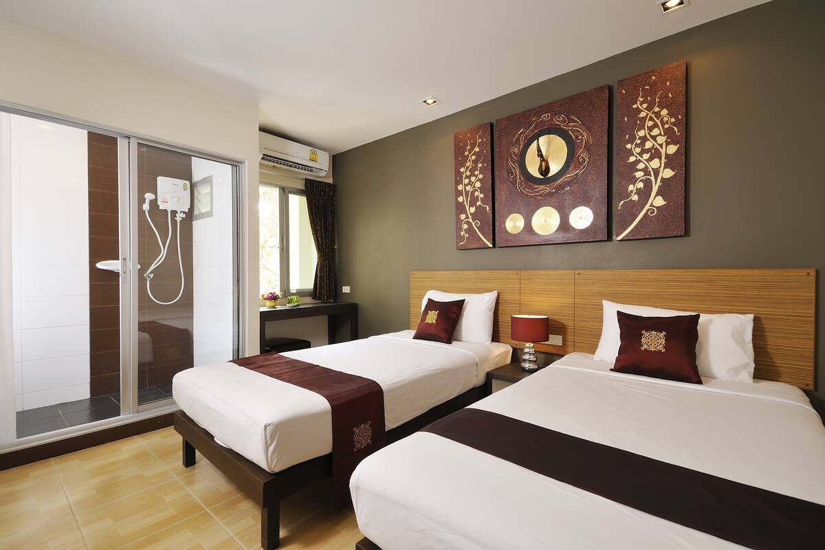 A hotel room with two beds, a shower area, and a desk with a computer.