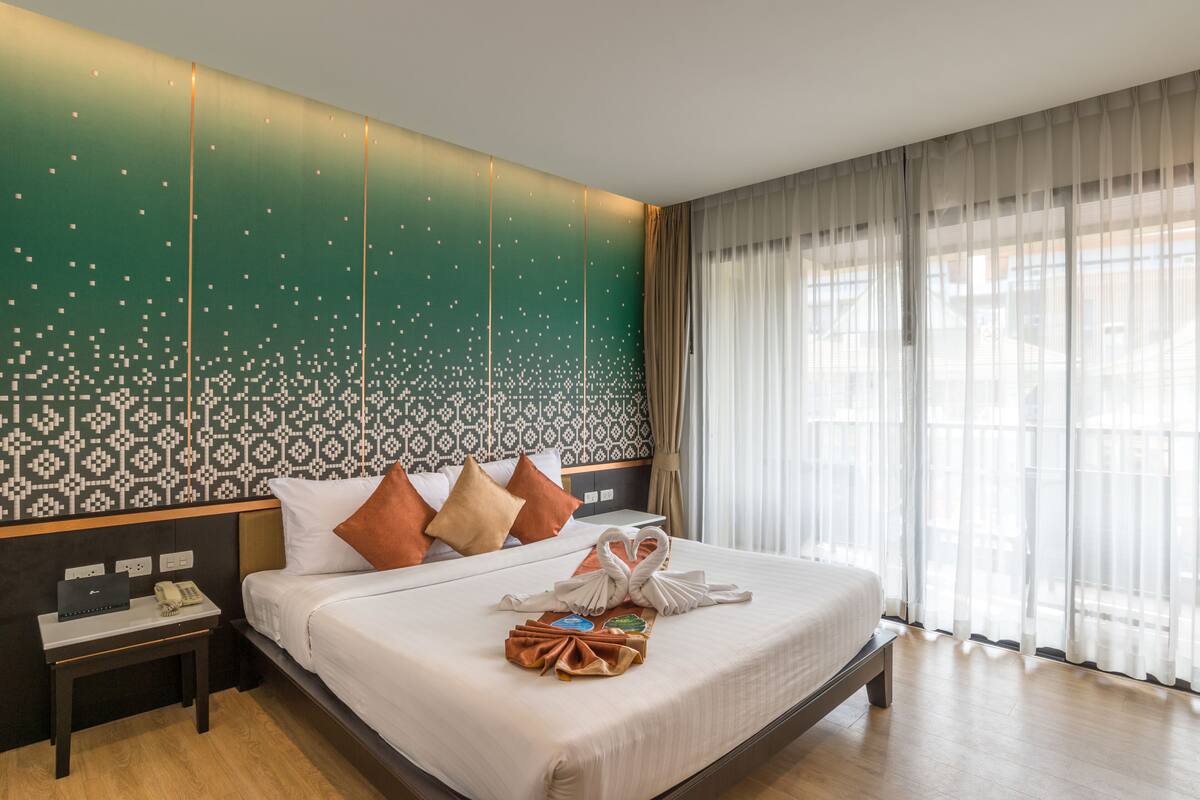A hotel room with a large bed, a bedside table with a phone, and a wall with a patterned design.