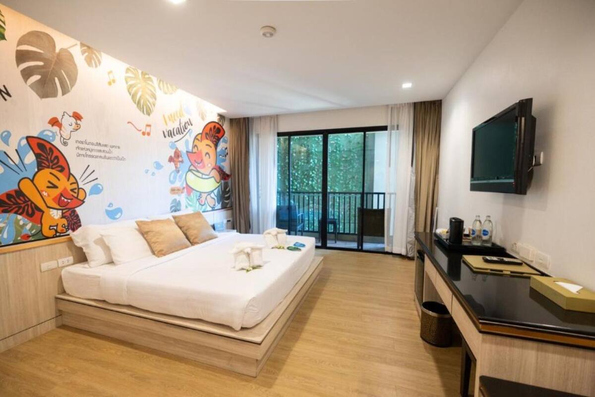A hotel room with a bed, a desk, a TV, and a balcony with a view of trees.