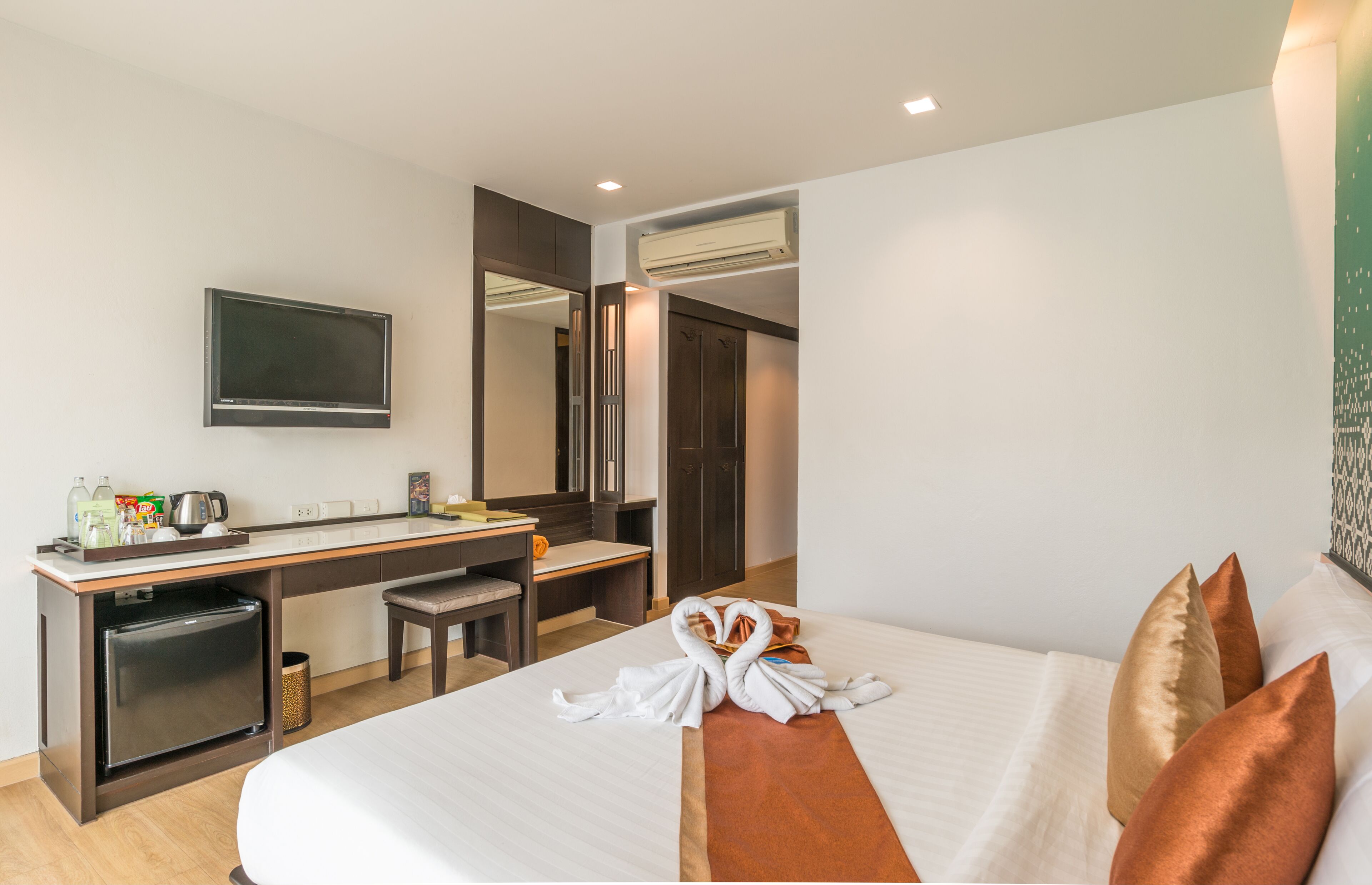 A hotel room with a bed, a desk, a television, a mirror, and a minibar.
