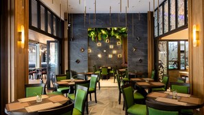 A restaurant with round tables and green chairs, a stone wall with hanging lights, and a view through a glass door. - Ananta Burin Resort (Krabi)