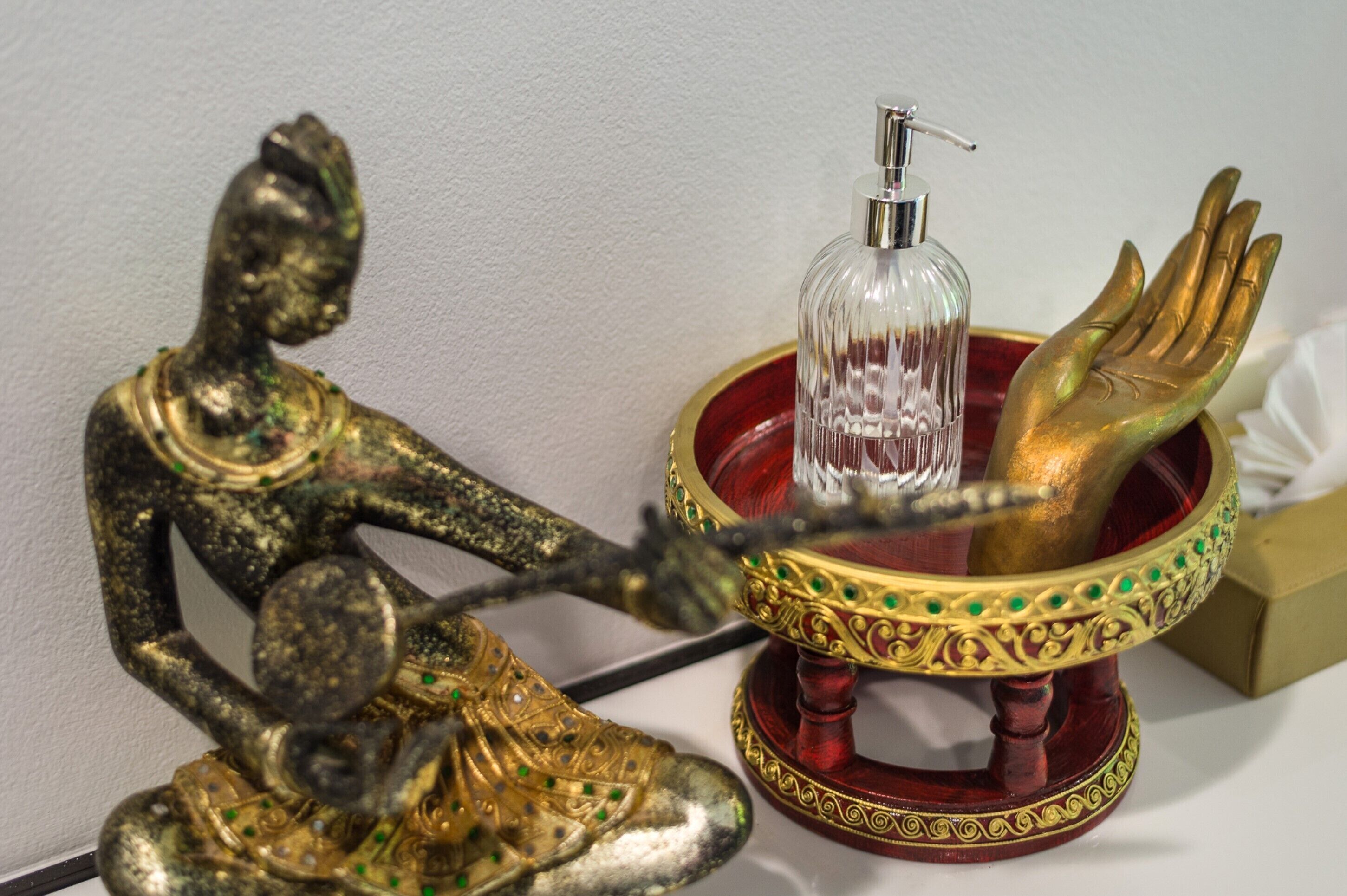 A statue of a seated figure next to a decorative bowl with a hand and a clear bottle.