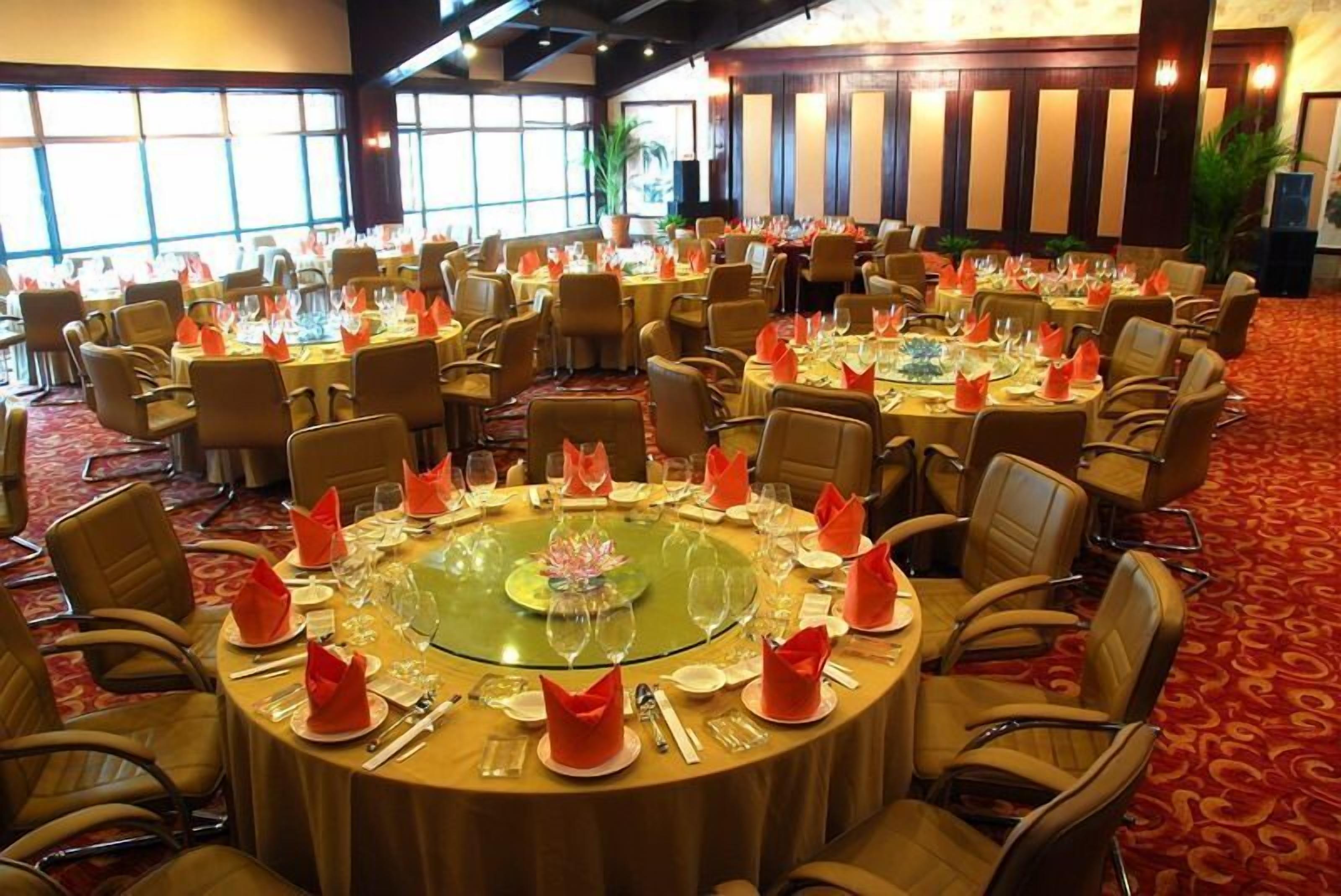 Un salón de banquetes con mesas redondas dispuestas para un evento formal, con centros de mesa de vidrio transparente y servilletas rojas.