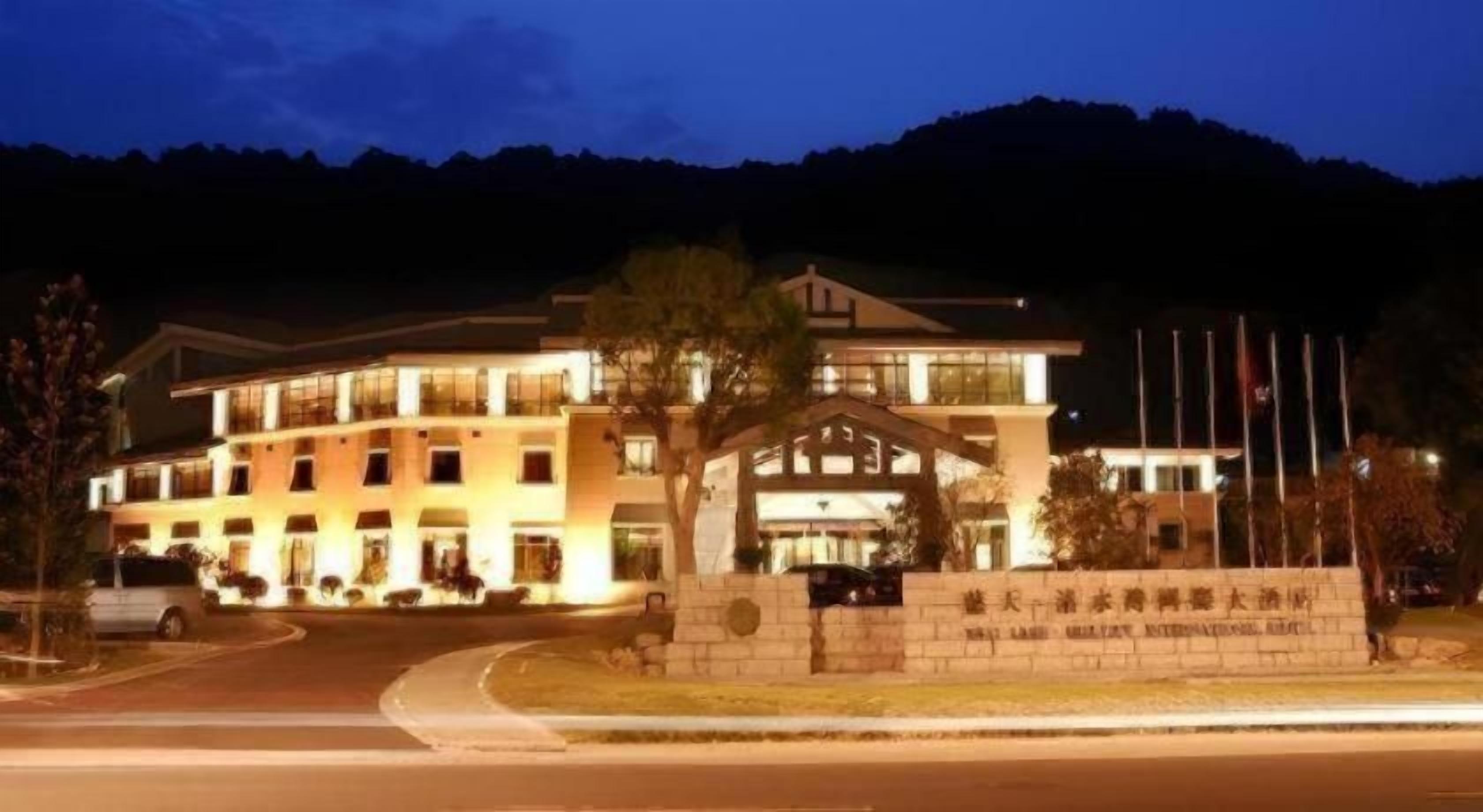 A multi-story hotel with a prominent entrance, a landscaped front yard, and a mountain backdrop.