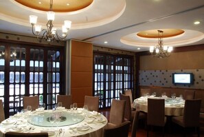 A dining area with round tables, chairs, chandeliers, and a television screen on the wall. - West Lake Hillview International Hotel (Hangzhou)