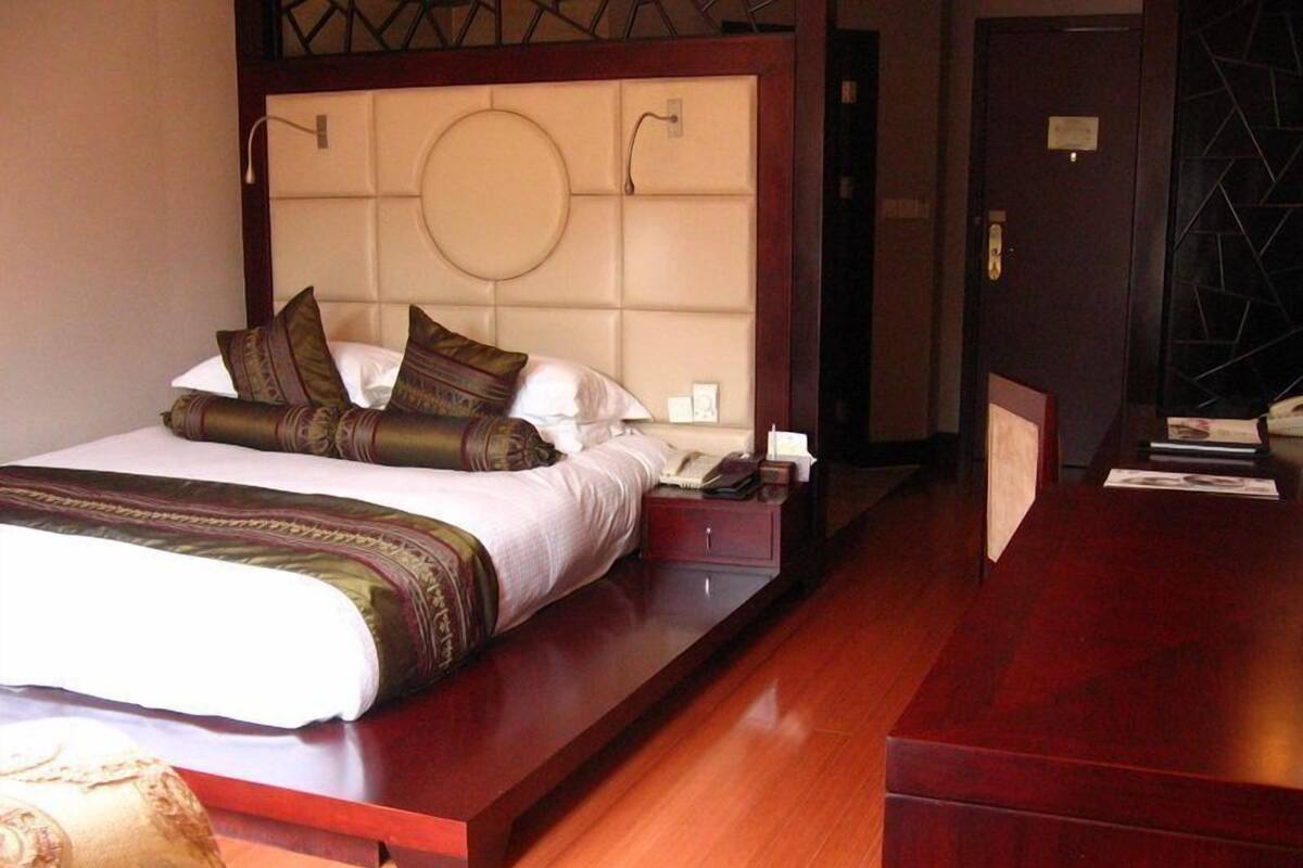 A hotel room with a large bed, a wooden desk, and a nightstand.