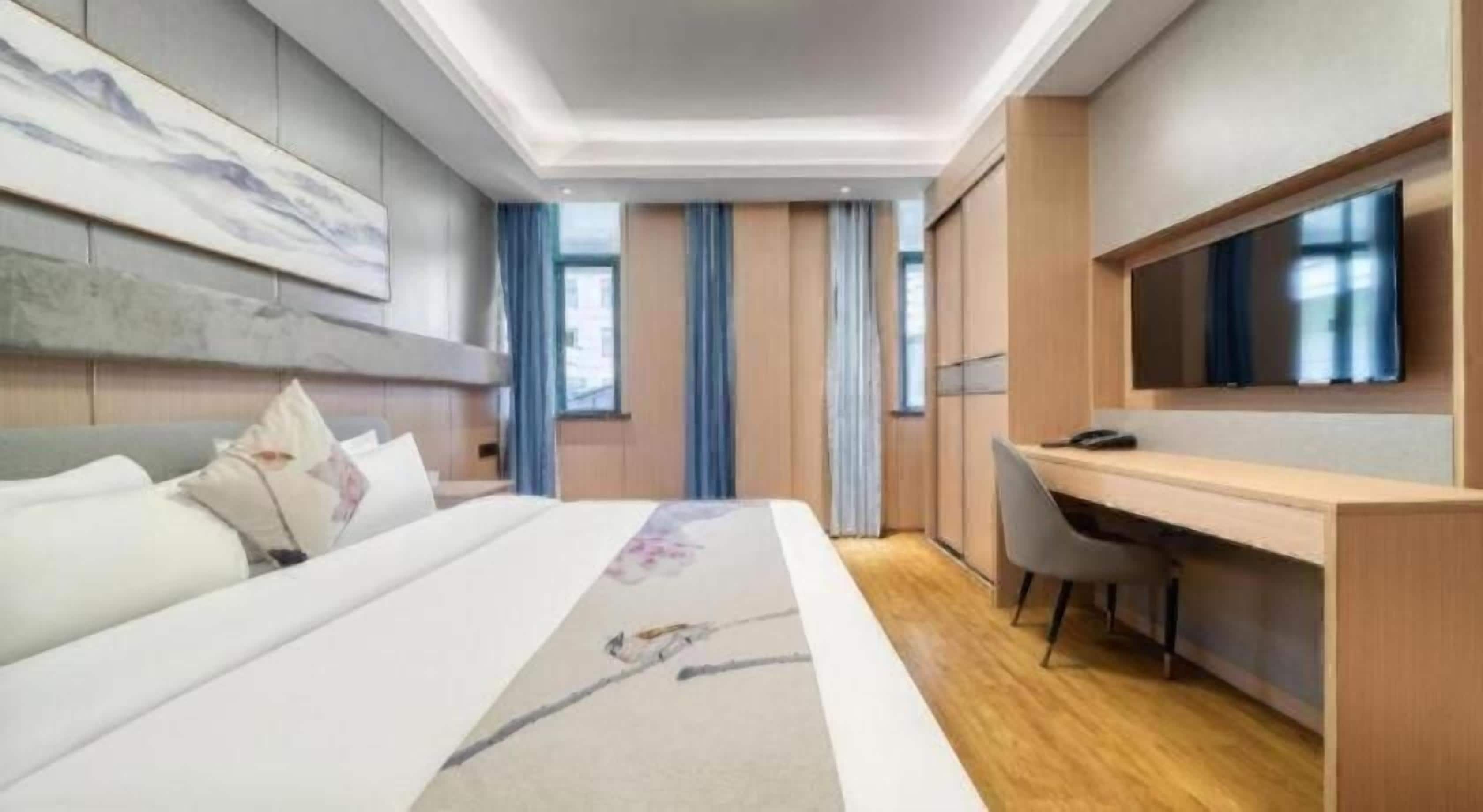 Quarto de hotel com cama, escrivaninha, cadeira, televisão e janela com cortinas.