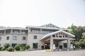 A large, modern building with a prominent entrance, multiple windows, and a landscaped area with trees and a statue. - West Lake Hillview International Hotel (Hangzhou)