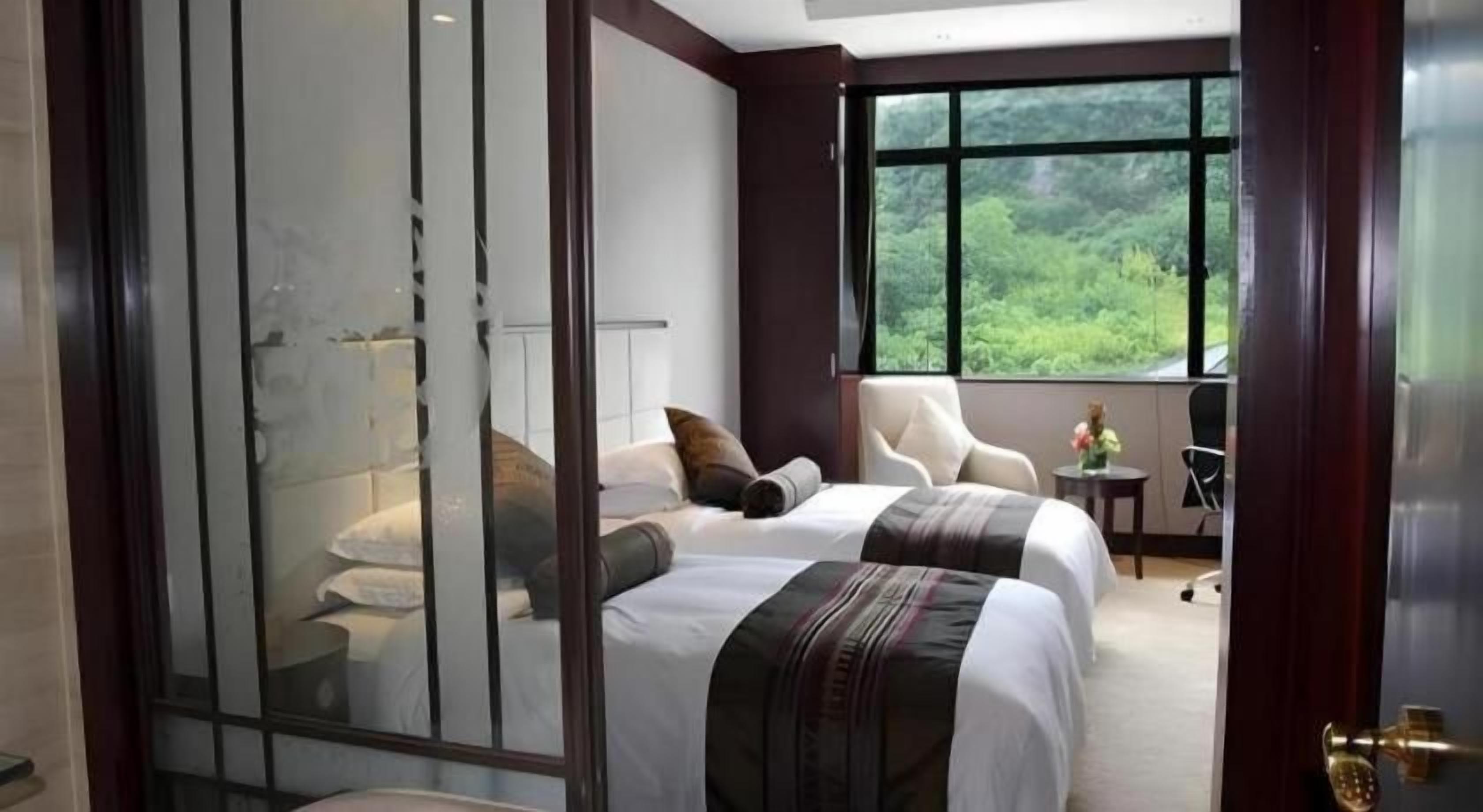 Une chambre d’hôtel avec deux lits, une grande fenêtre donnant sur un espace verdoyant et une porte-fenêtre coulissante.