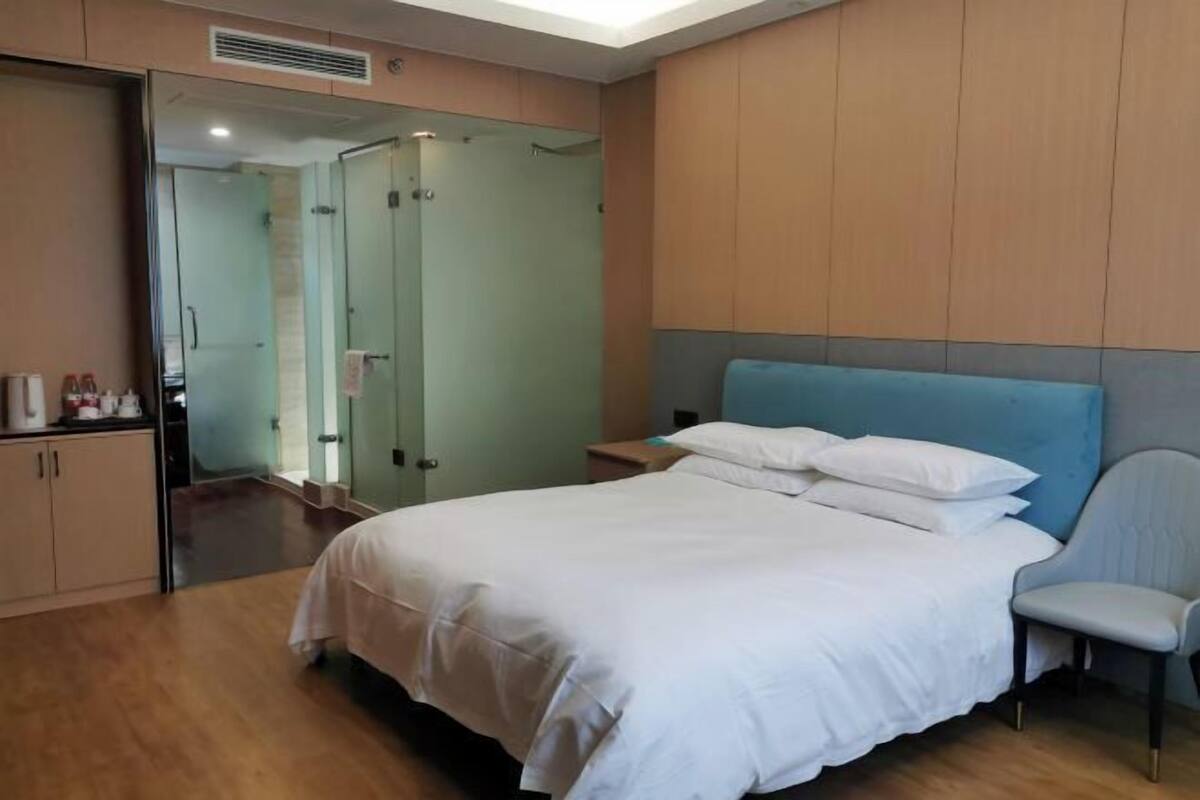 A hotel room with a bed, a chair, a nightstand, a mirror, and a wardrobe.