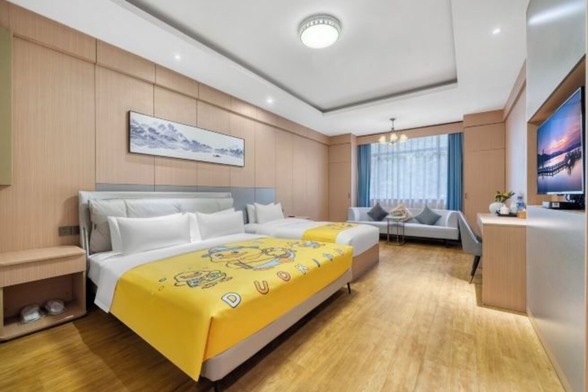 Habitación de hotel con cama, escritorio, silla, televisor y ventana con cortinas.