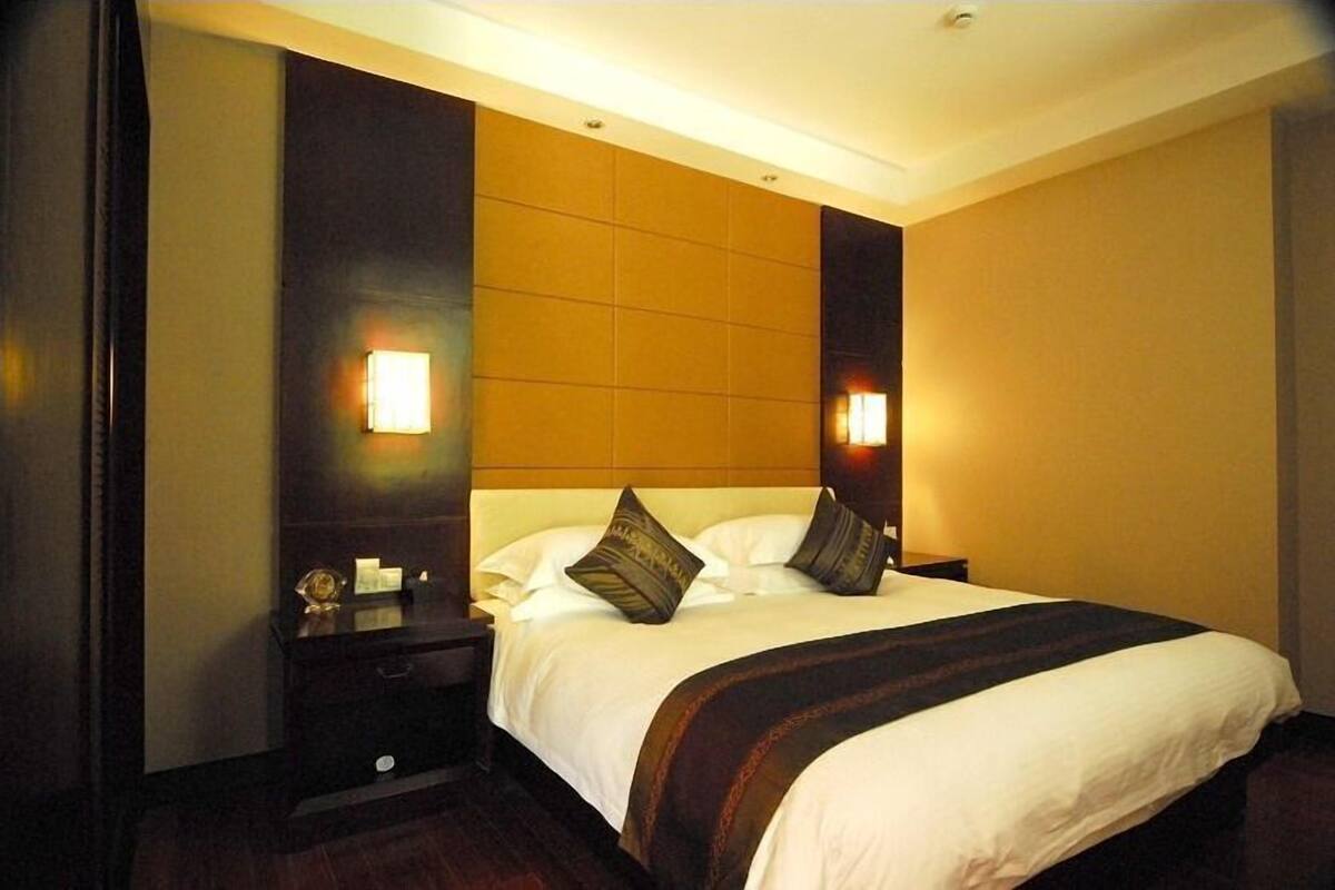 A hotel room with a large bed, two bedside tables, and wall-mounted lamps.