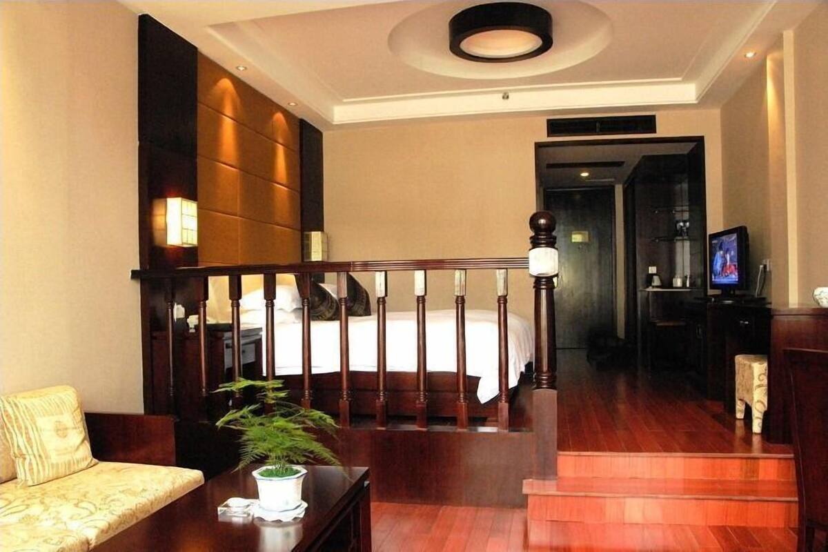 A hotel room with a wooden staircase, a bed with white bedding, a sofa, a small table with a plant, and a television on a stand.