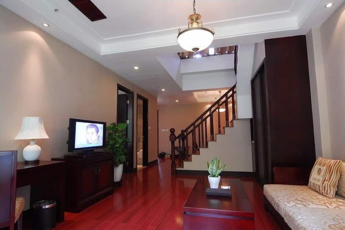 A spacious living room with a wooden floor, a television, a sofa, and a staircase leading to another level.