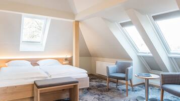 Une chambre à coucher comprenant un lit, des tables de chevet, un banc, une petite table ronde et deux chaises. Elle est dotée de fenêtres de toit et d’une fenêtre qui laissent entrer la lumière naturelle.