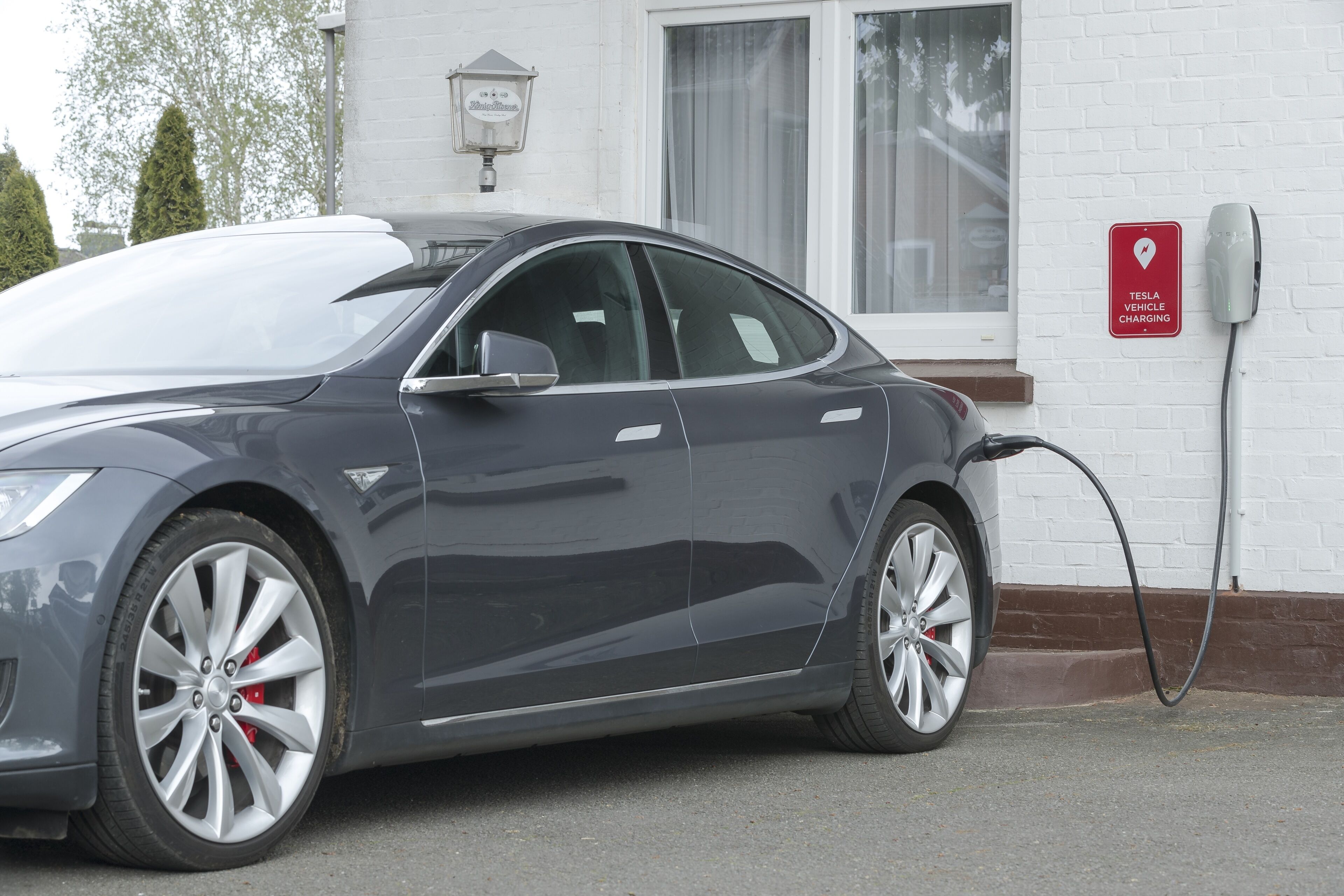 A Tesla charging station with a white brick wall and a window in the background.