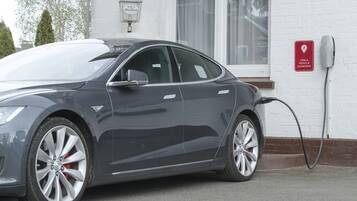 A Tesla charging station with a white brick wall and a window in the background.