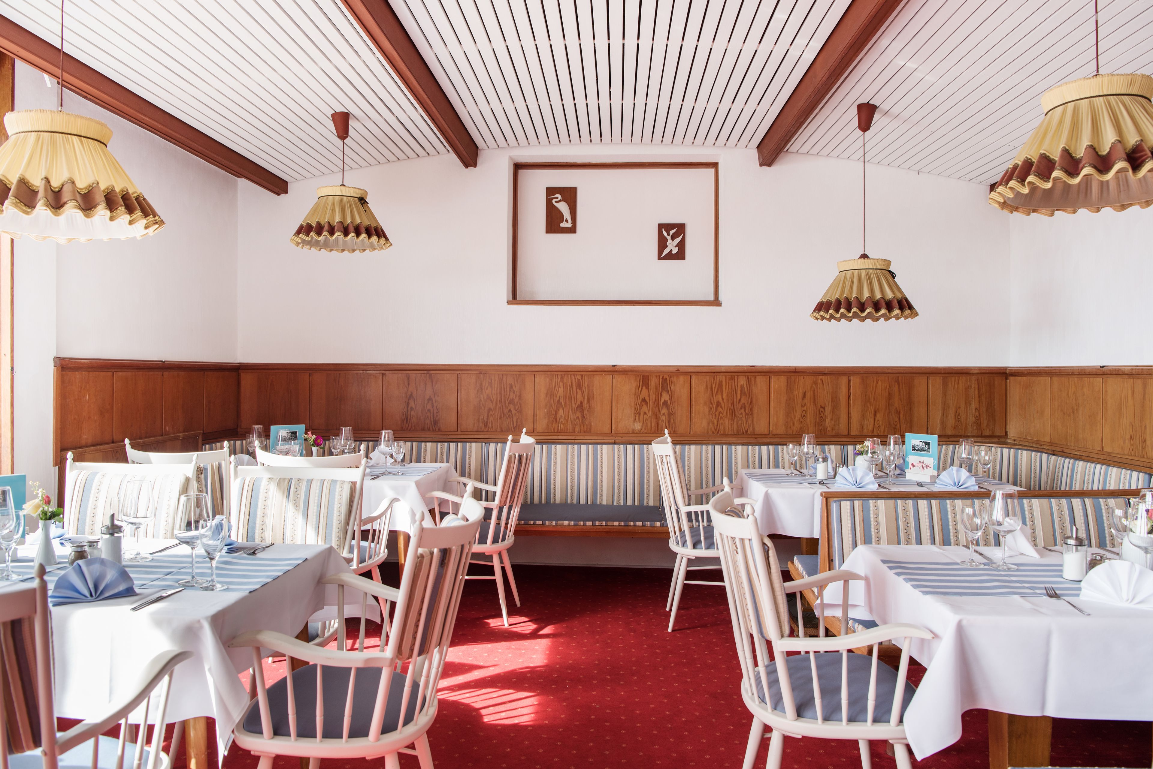 A dining area with tables set for service, wooden paneling on the walls, and hanging lamps.