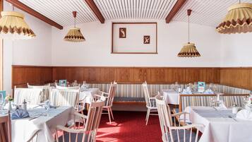 A dining area with tables set for service, wooden paneling on the walls, and hanging lamps.