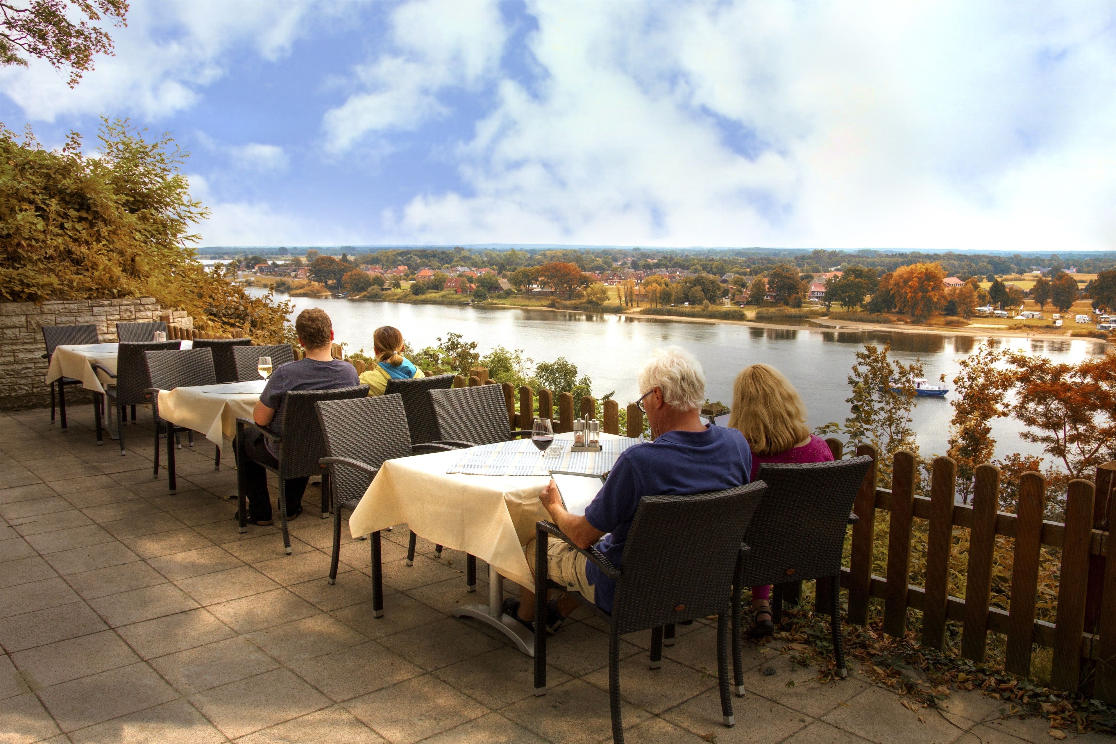 Een buitenterras met tafels en stoelen met uitzicht op een rivier.