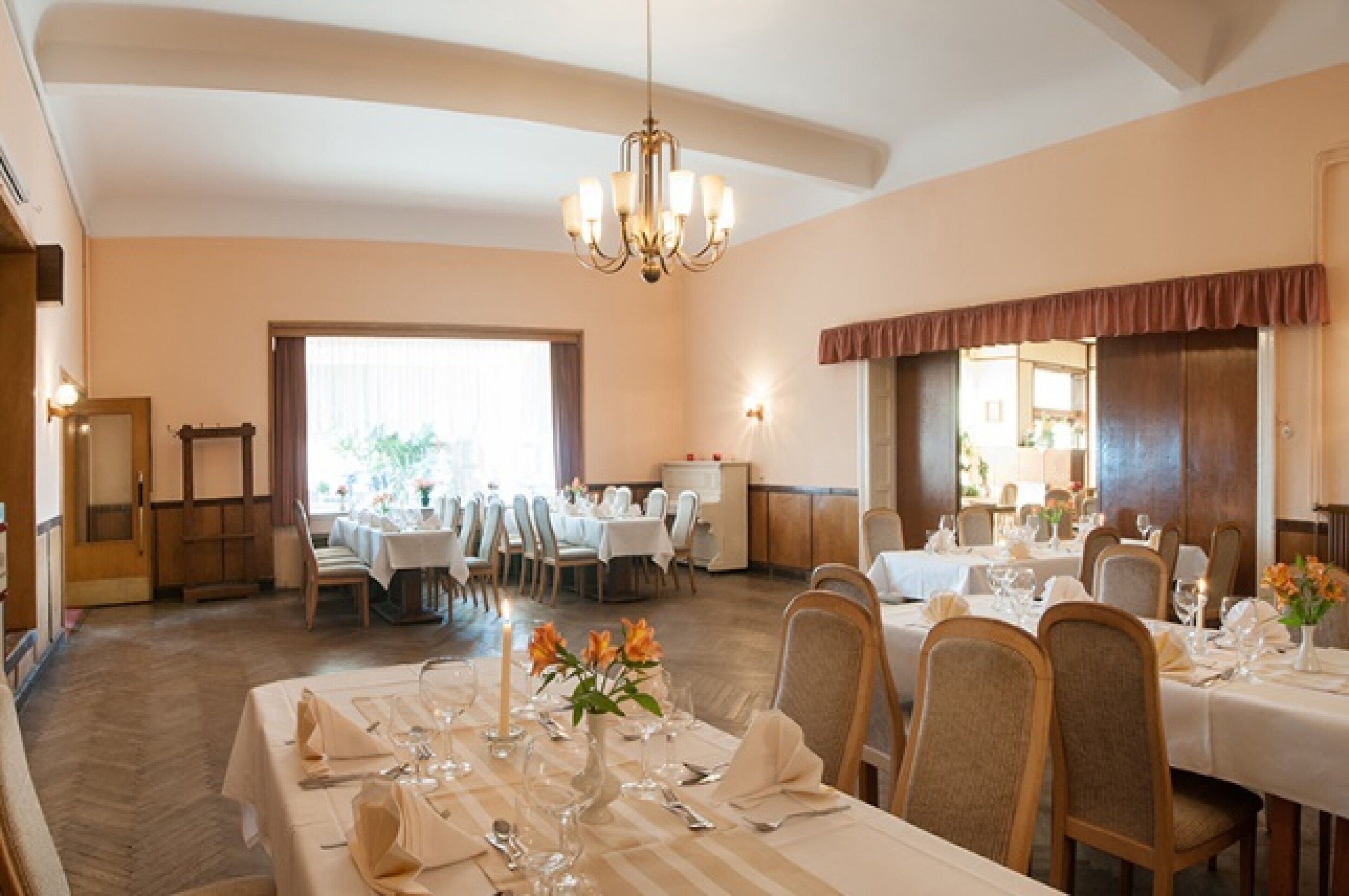 A dining area with multiple tables set for service, a chandelier, and a view of the outdoors.