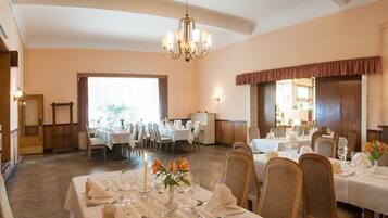 A dining area with multiple tables set for service, a chandelier, and a view of the outdoors.