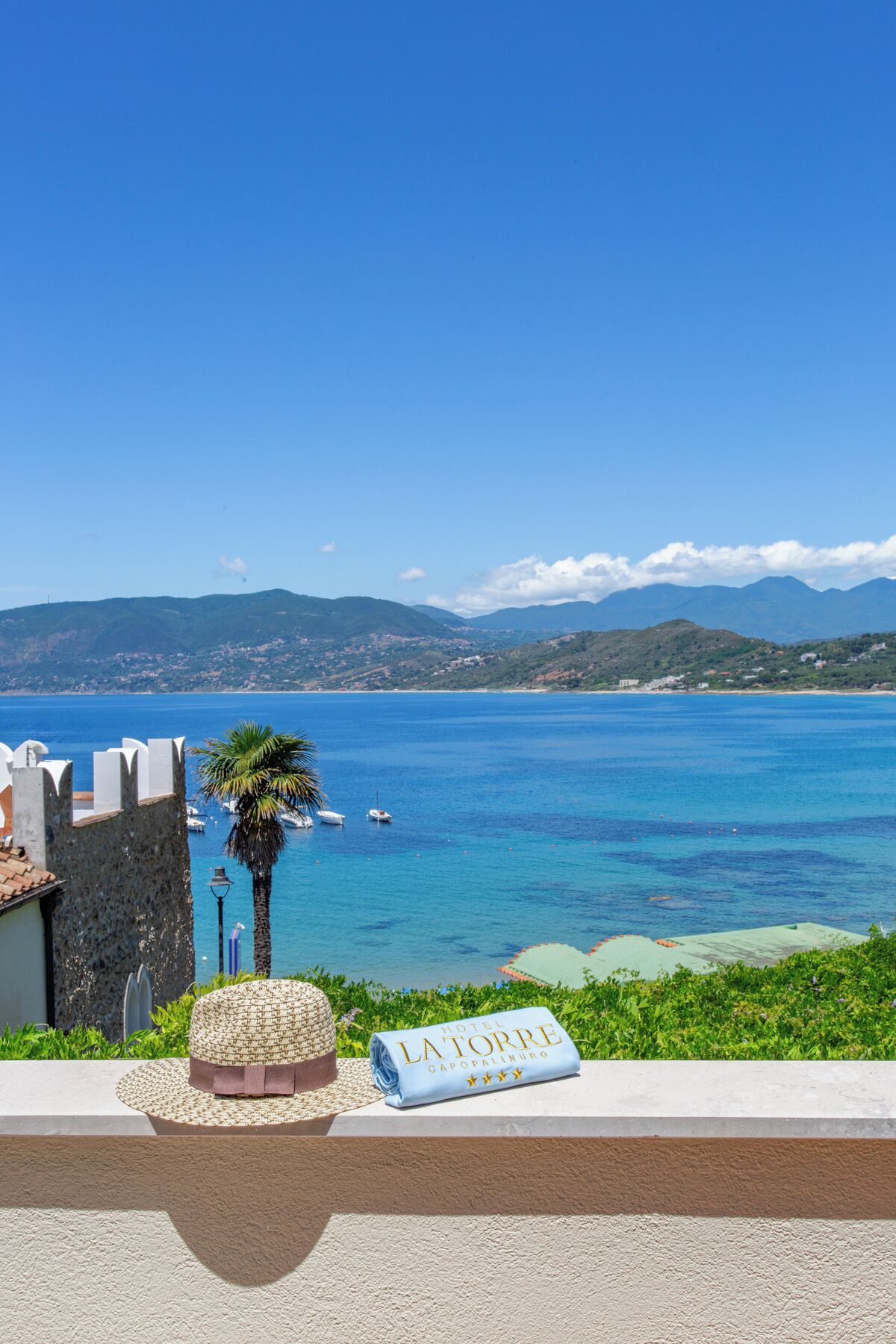 Blick auf die Küste mit blauem Himmel, einer Palme und einem Schild für Hotel La Torre Capopalmuro.