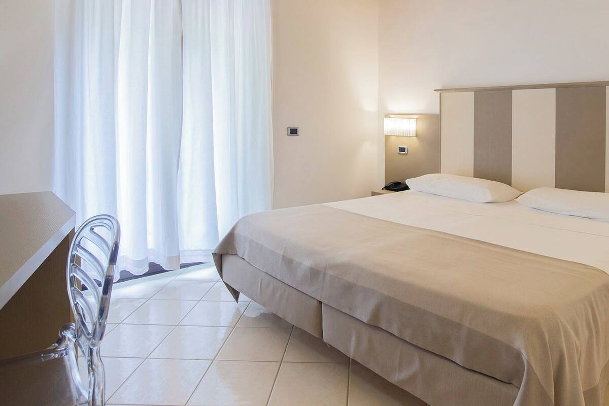A hotel room with a large bed, bedside tables, a desk, and a chair.