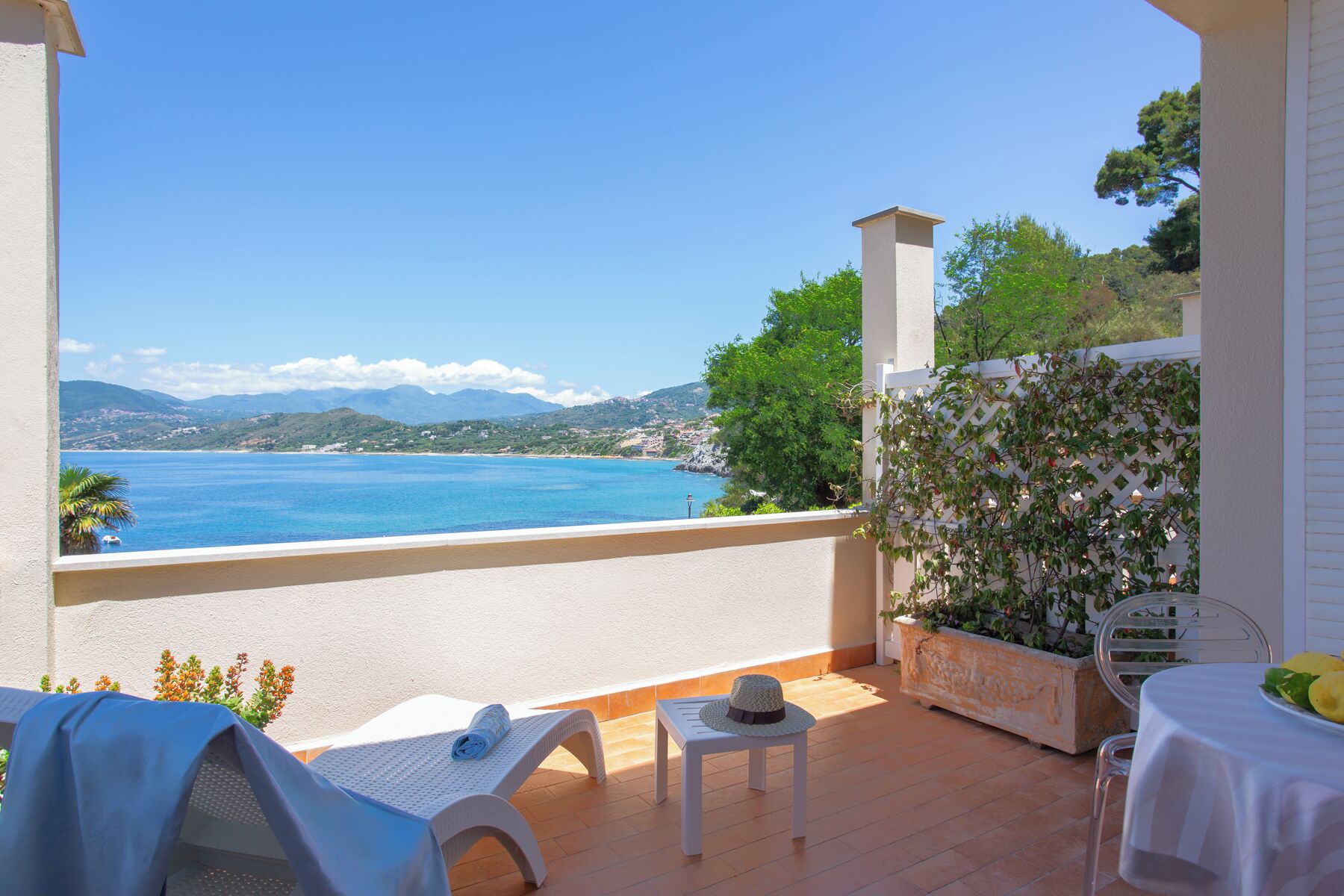 A balcony with a view of the sea, a table with a hat, and a chair.