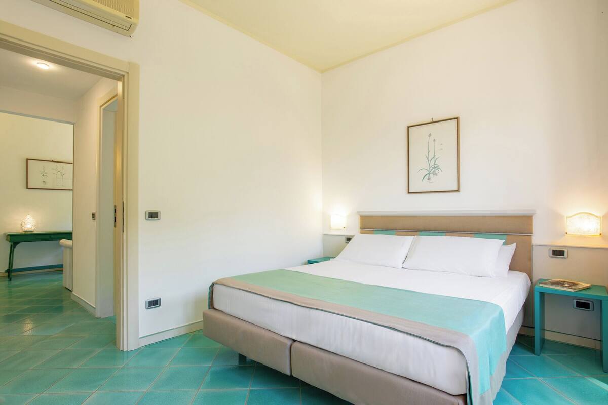 A bedroom with a bed, bedside tables, a nightstand, a mirror, and a door.