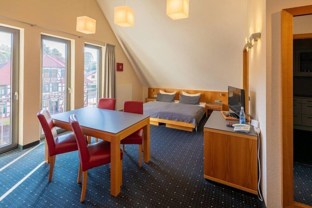Una habitación con cama, escritorio, silla, mesa y un ventanal grande.