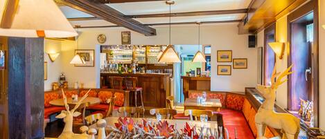 A cozy restaurant with wooden beams, red upholstered seating, and a deer sculpture.