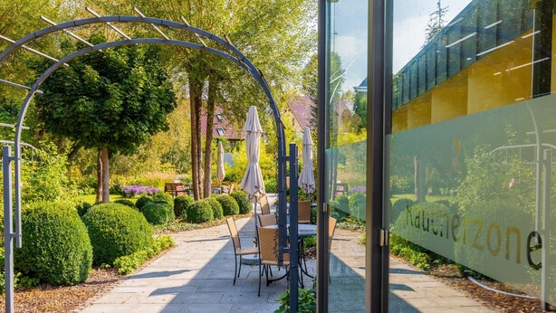 An outdoor seating area with tables and chairs, surrounded by neatly trimmed hedges and trees. - Gasthaus Goldener Hirsch (Suhl)