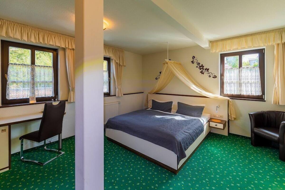 Un dormitorio con cama, escritorio, silla y ventana con cortinas.