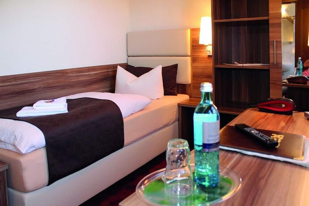 Habitación de hotel con cama, mesita de noche, lámpara y una bandeja con botella y vaso.
