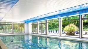 An indoor swimming pool with clear glass walls, a tiled floor, and a view of greenery outside. - Garden & City Capvern-les-Bains (Capvern)