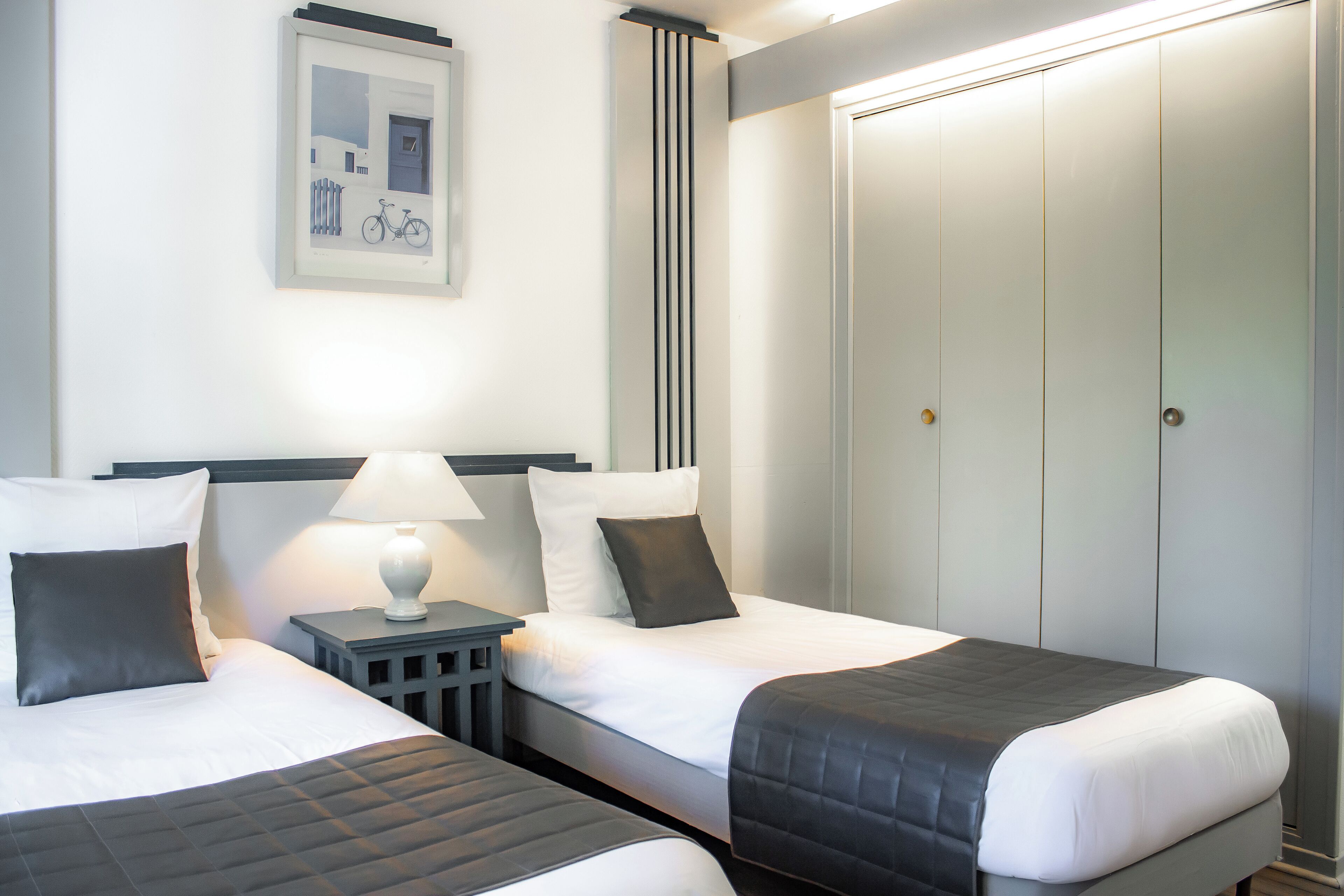 Een hotelkamer met twee bedden, een nachtkastje met een lamp, een lijst met een foto aan de muur, en een kledingkast.