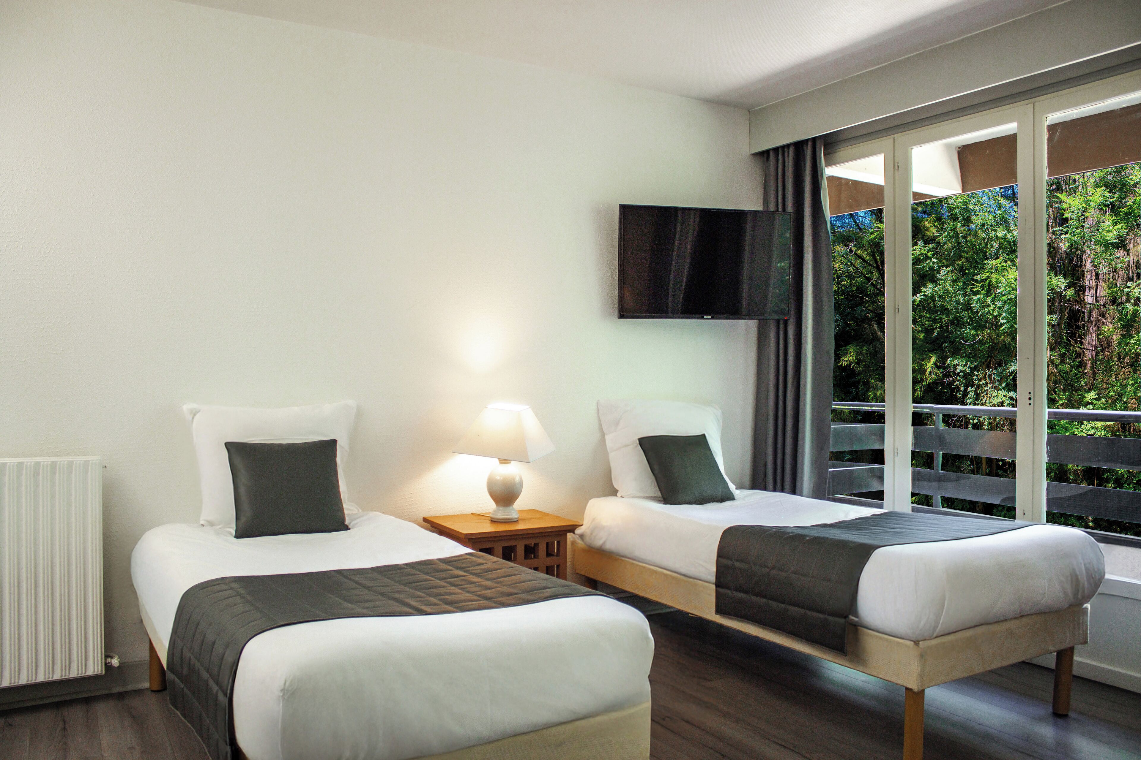 Une chambre d’hôtel avec deux lits, un téléviseur fixé au mur et une fenêtre donnant sur un paysage verdoyant.